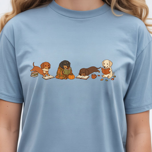 A light blue crewneck t-shirt featuring a graphic print of four cute cartoon dogs reading books, worn by a model.