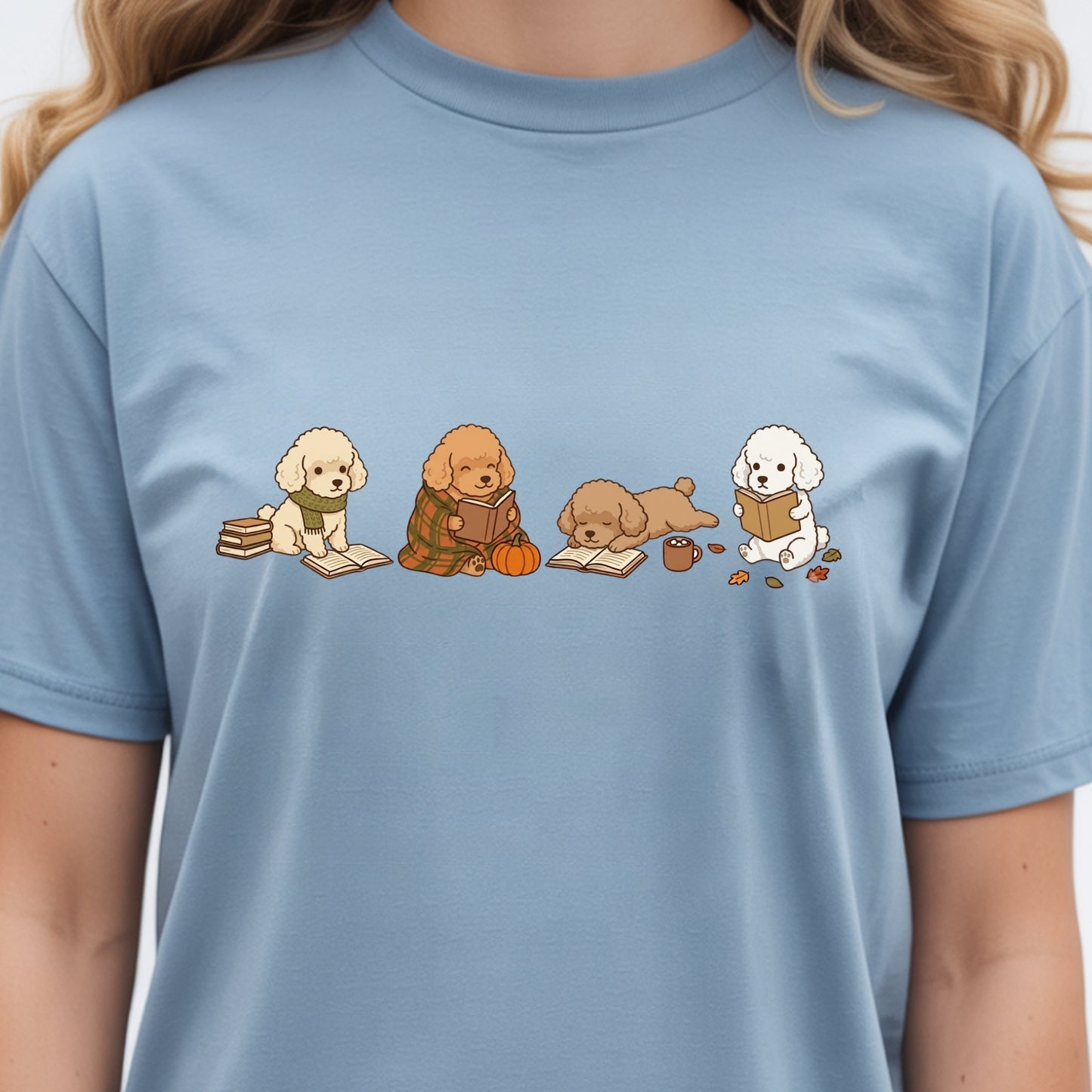 A light blue crewneck t-shirt featuring a graphic print of four cute cartoon poodles reading books, worn by a model.
