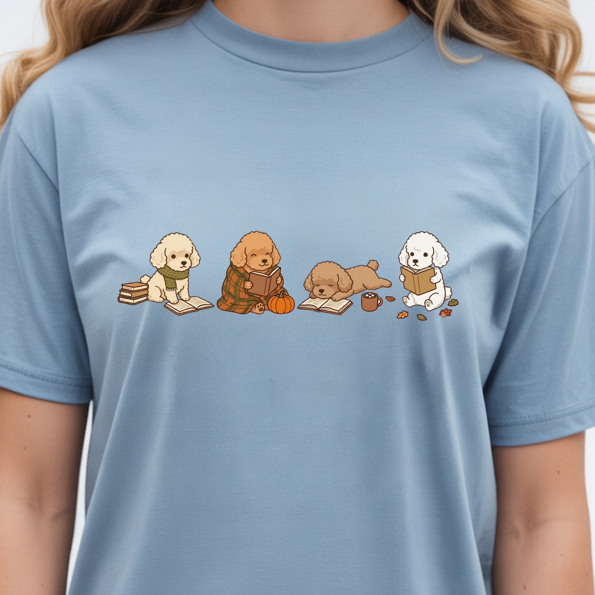A light blue crewneck t-shirt featuring a graphic print of four cute cartoon poodles reading books, worn by a model.