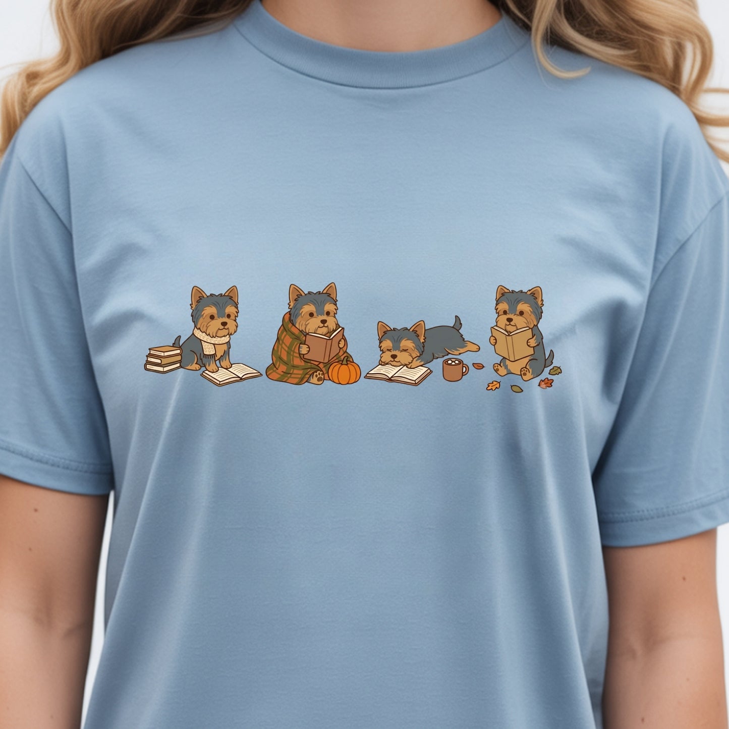 A person wearing a light blue crewneck t-shirt with a graphic print of four cartoon Yorkshire Terrier dogs reading books.