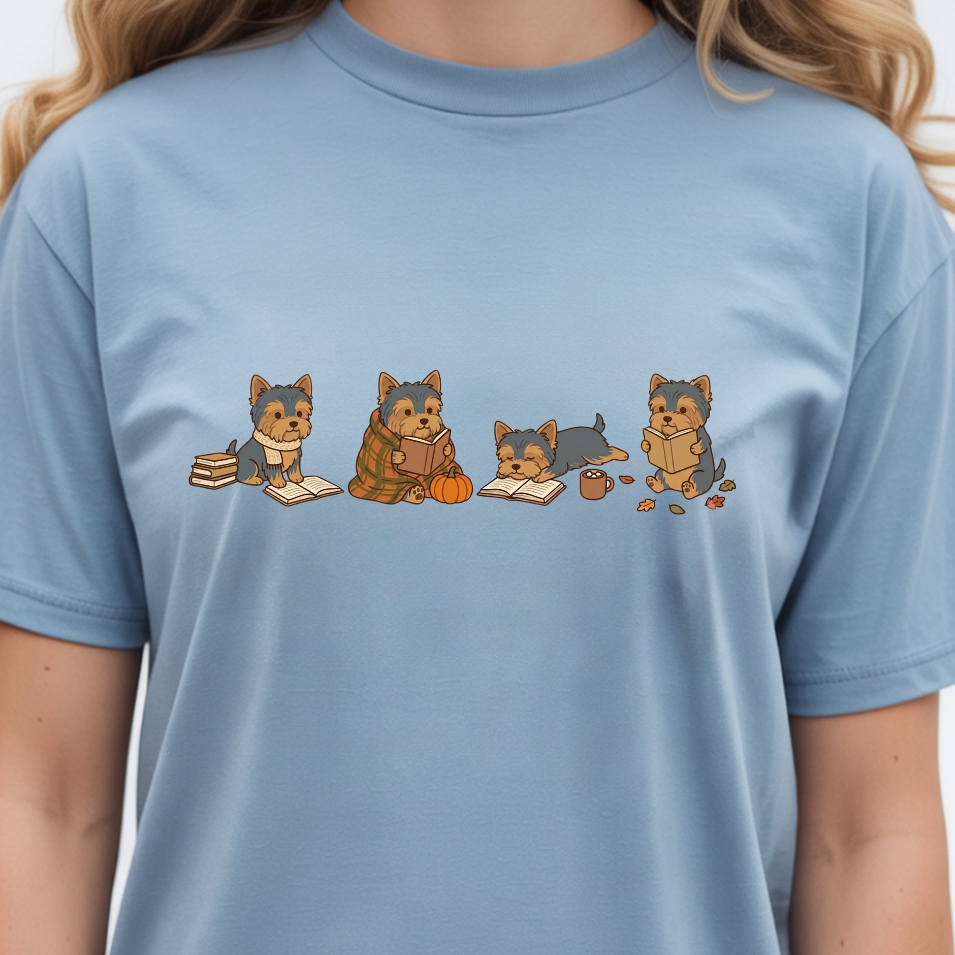 A person wearing a light blue crewneck t-shirt with a graphic print of four cartoon Yorkshire Terrier dogs reading books.