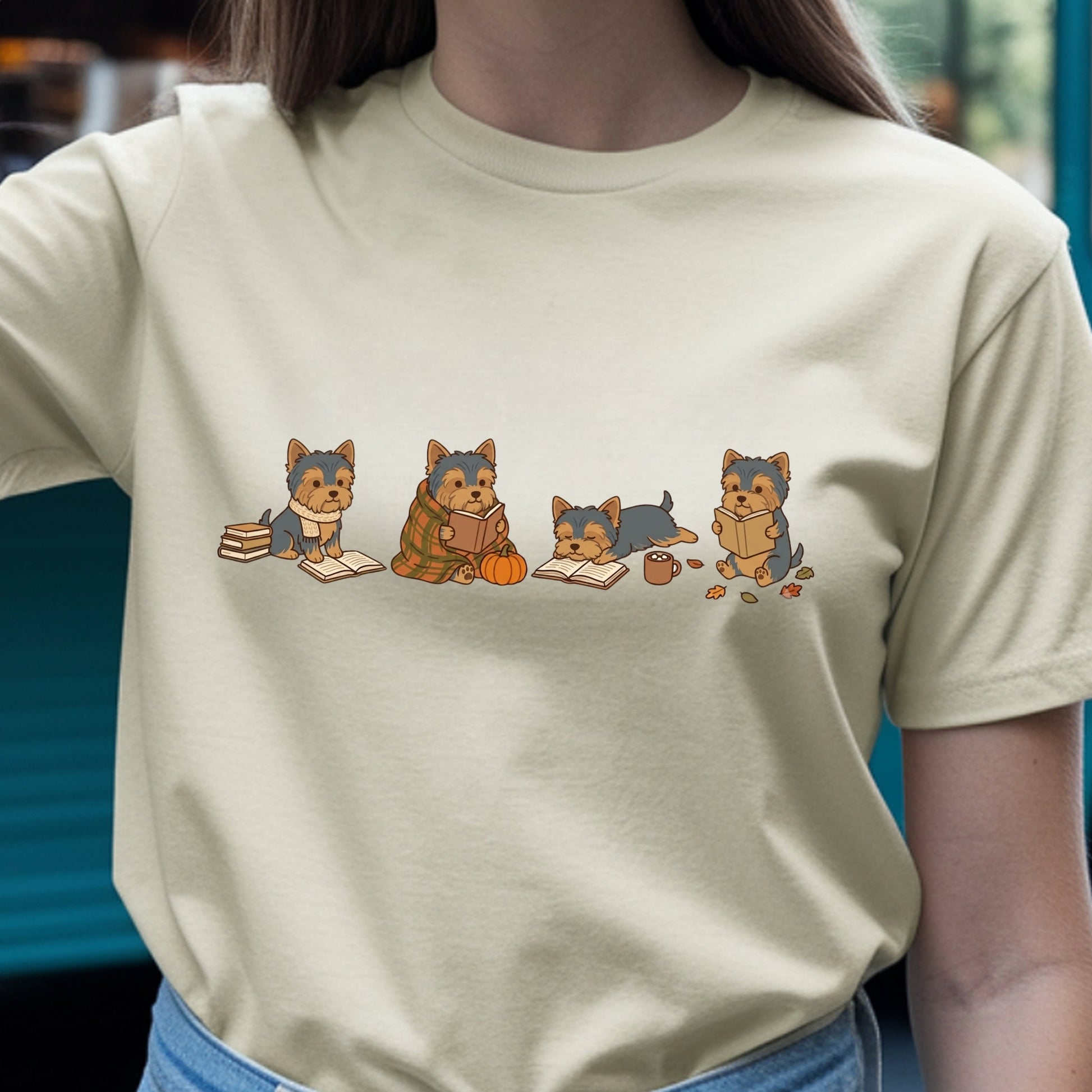 A person wearing a light beige short-sleeve t-shirt with a graphic of four cute cartoon dogs reading books, paired with blue jeans.