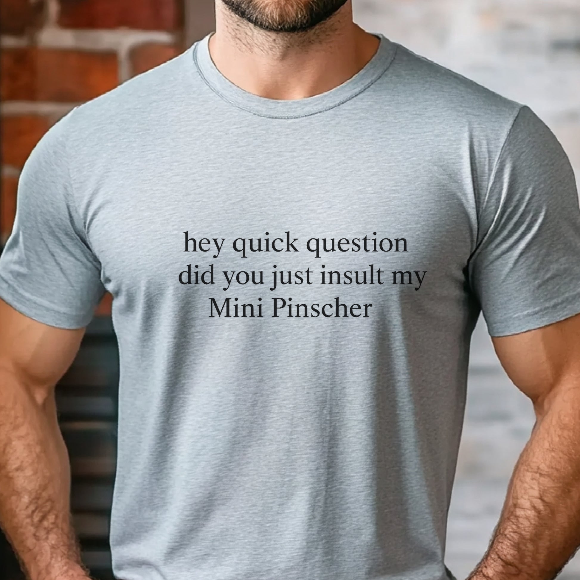 Man wearing a grey "hey quick question did you just insult my Mini Pinscher" t-shirt, standing by a window