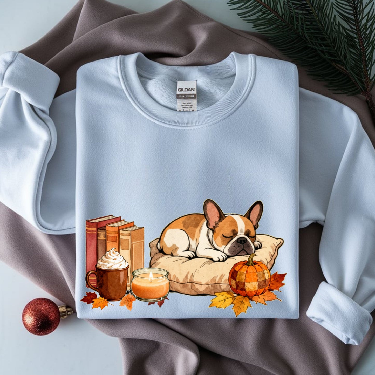 Folded sweatshirt with a dog, books, pumpkin, and leaves design on a fabric background