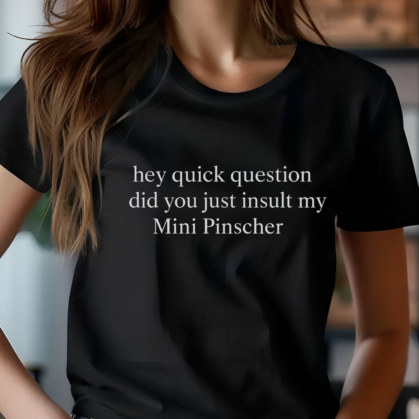 Woman wearing a black "hey quick question did you just insult my Mini Pinscher" t-shirt, standing by a window
