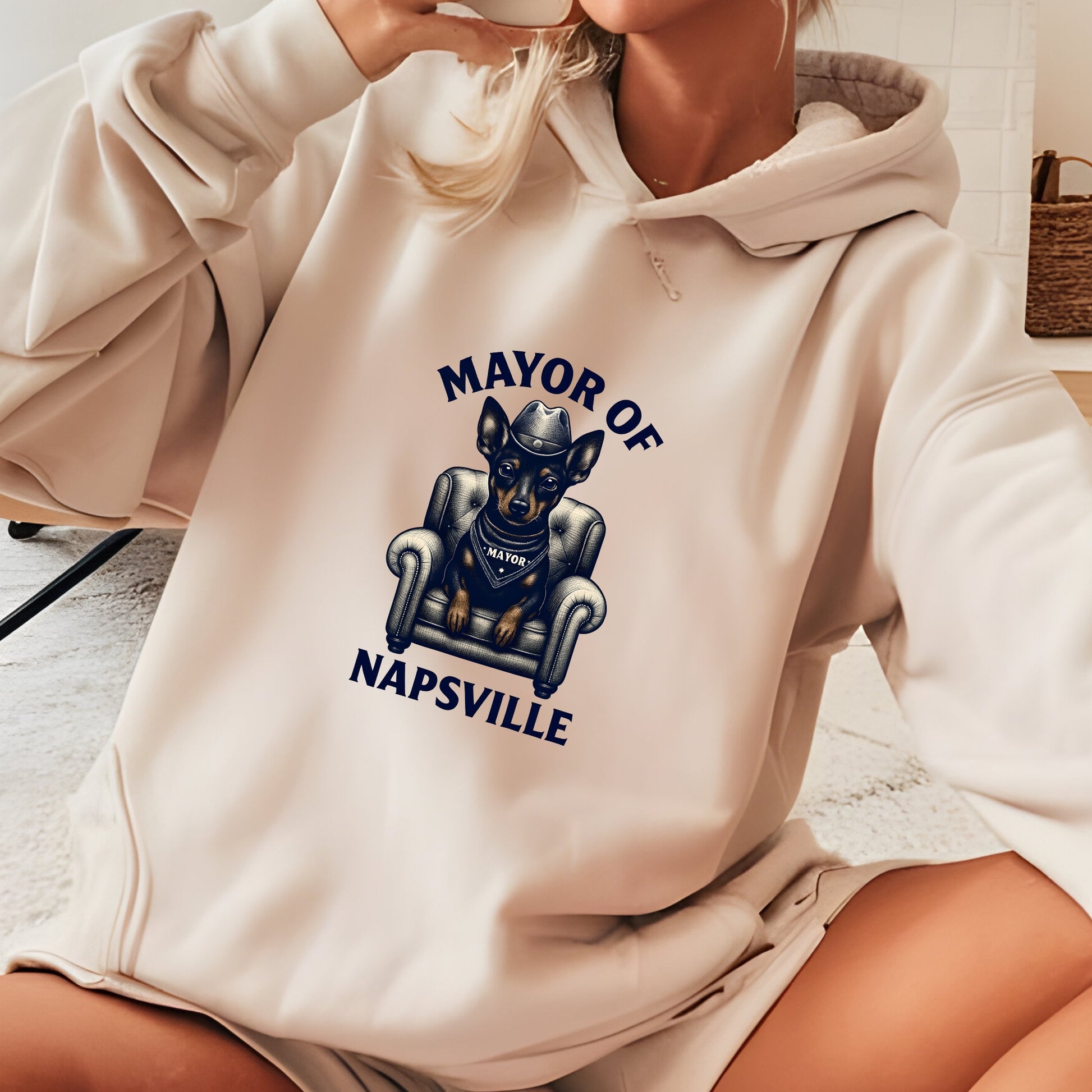 Woman wearing a sand "Mayor of Napsville" Miniature Pinscher hoodie with a dog on an armchair and funny nap design