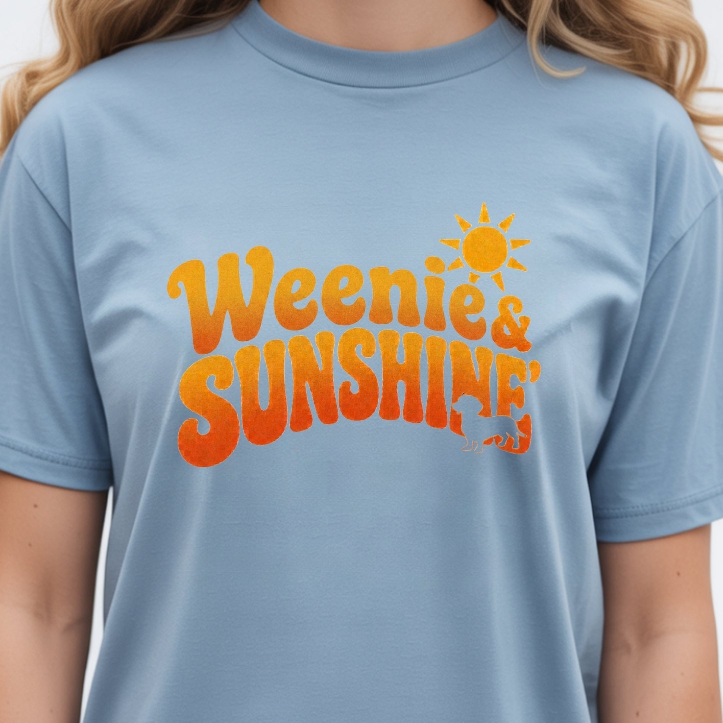 A light blue crewneck t-shirt featuring a retro-style orange graphic that reads 'Weenie & Sunshine' with a sun icon, worn by a model.