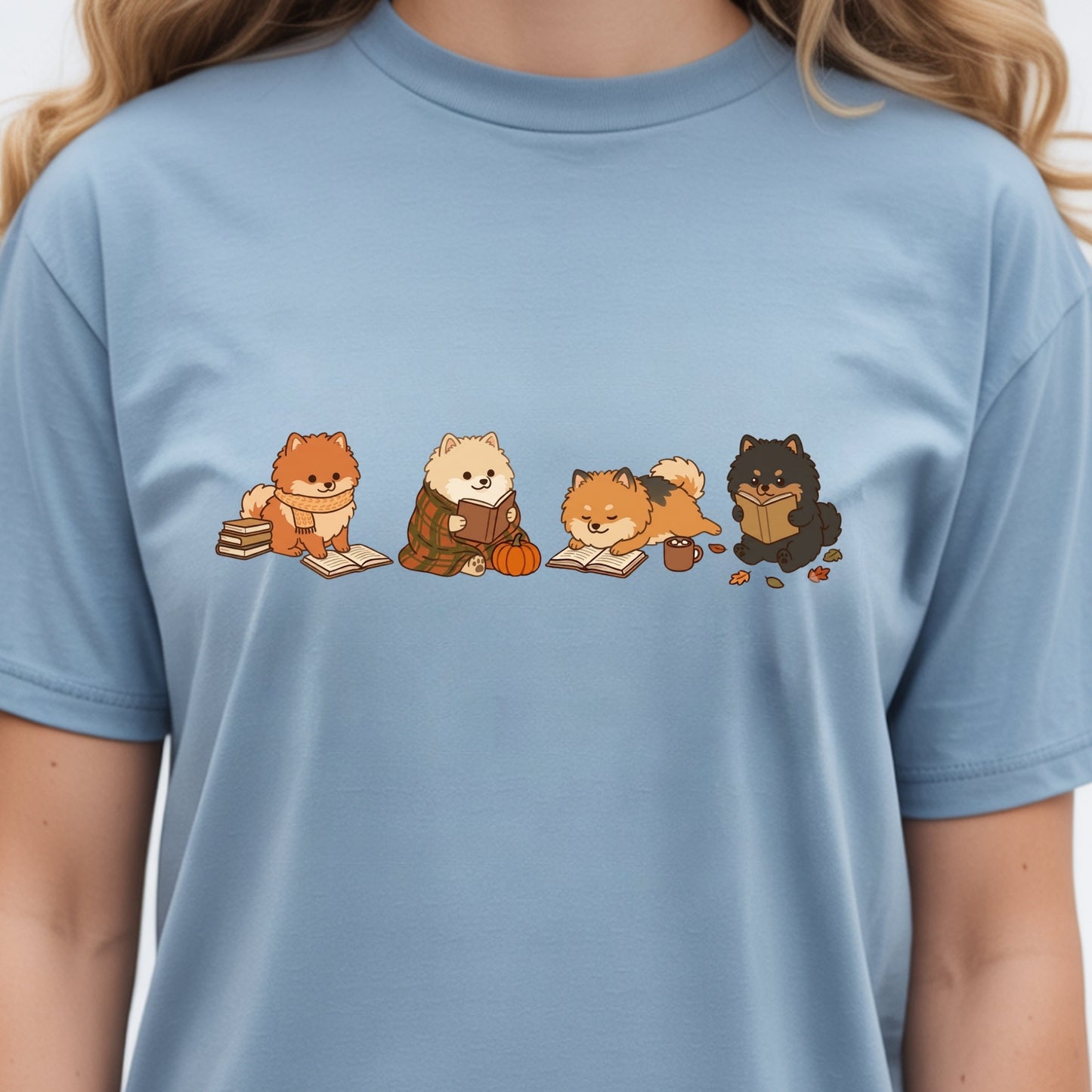 A person wearing a light blue crewneck t-shirt with a graphic print of four cute cartoon dogs reading books.