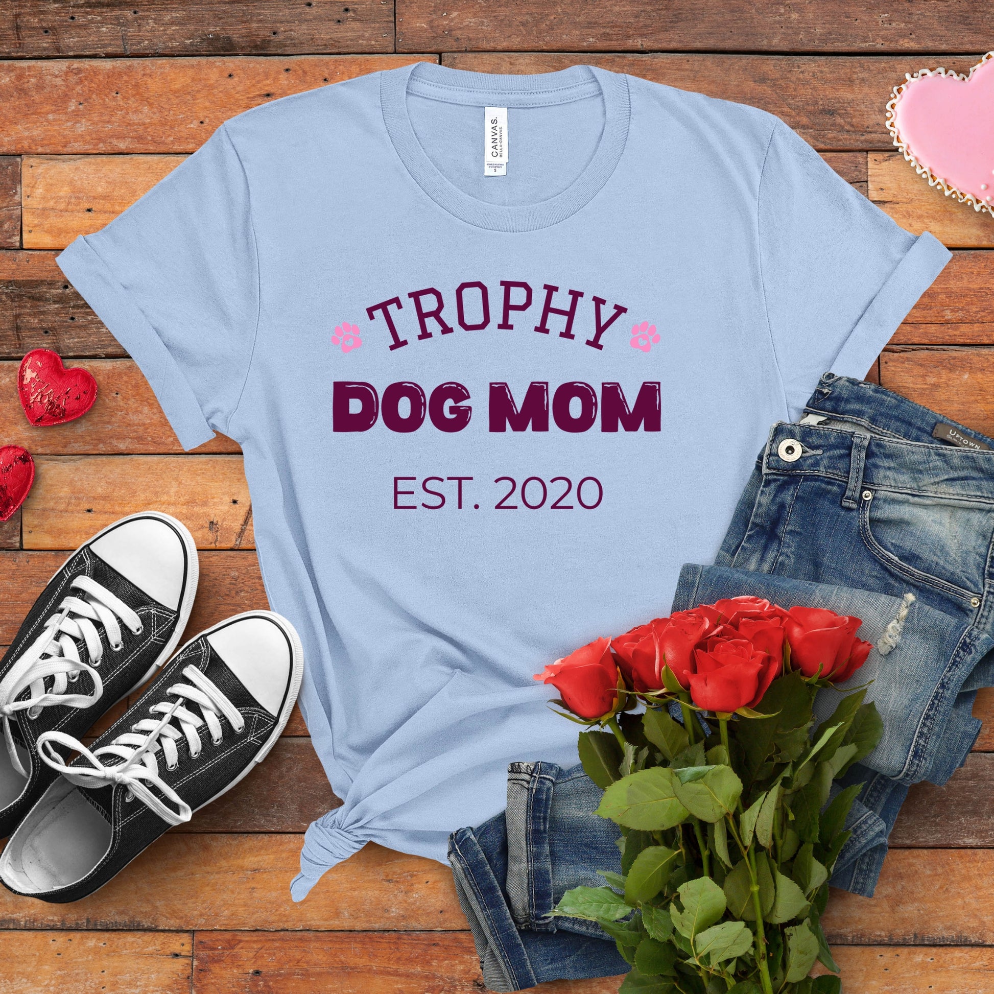 Light blue t-shirt with 'Trophy Dog Mom Est. 2020' text on a wooden surface with jeans, sneakers, and roses.