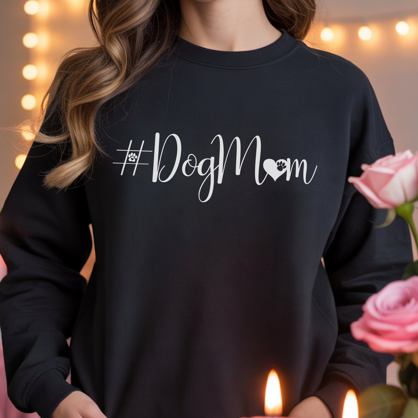 Person wearing a black sweatshirt with '#DogMom' text, holding pink roses and candles.