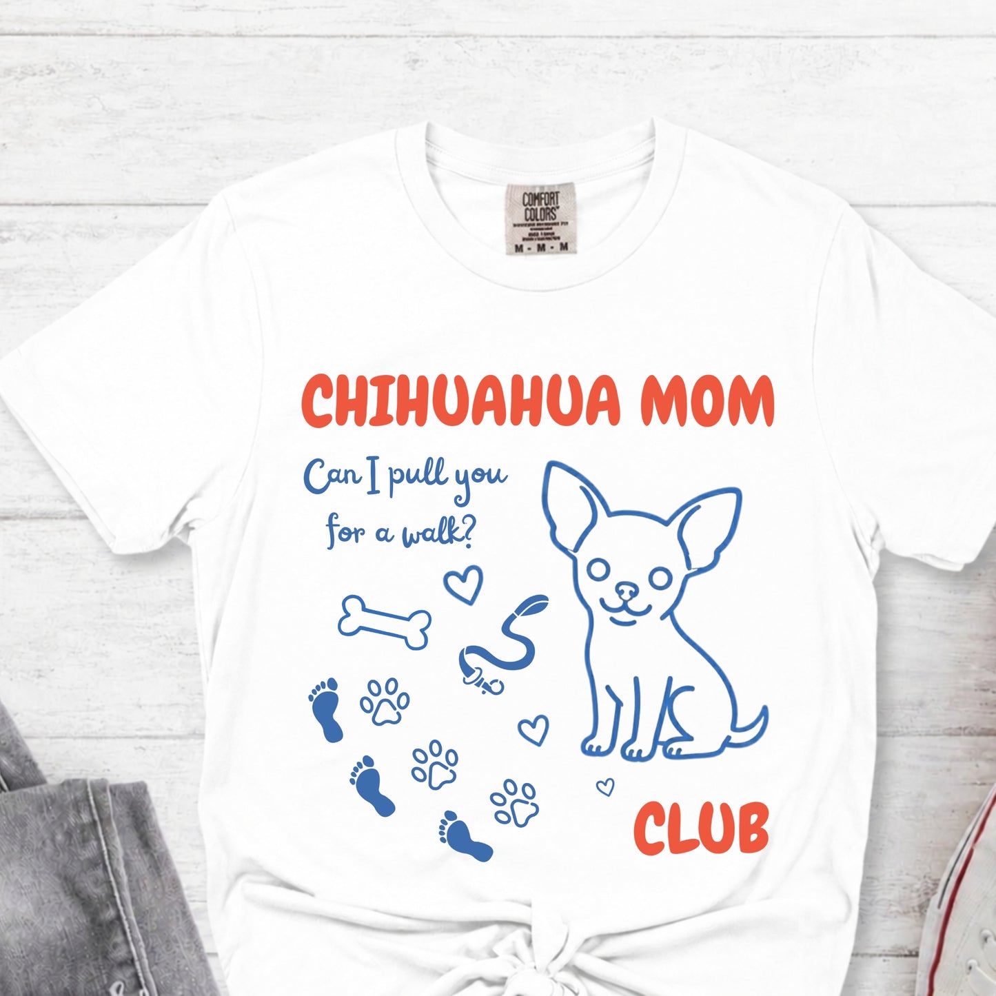 White t-shirt with 'Chihuahua Mom Club' text and graphics on a light wooden surface.