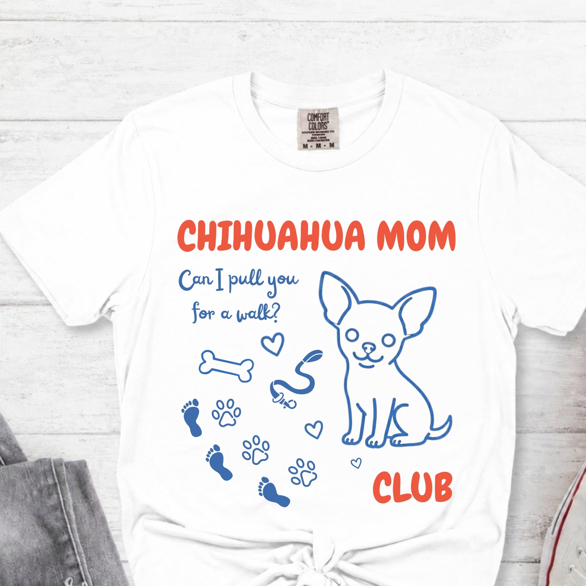 White t-shirt with 'Chihuahua Mom Club' text and graphics on a light wooden surface.
