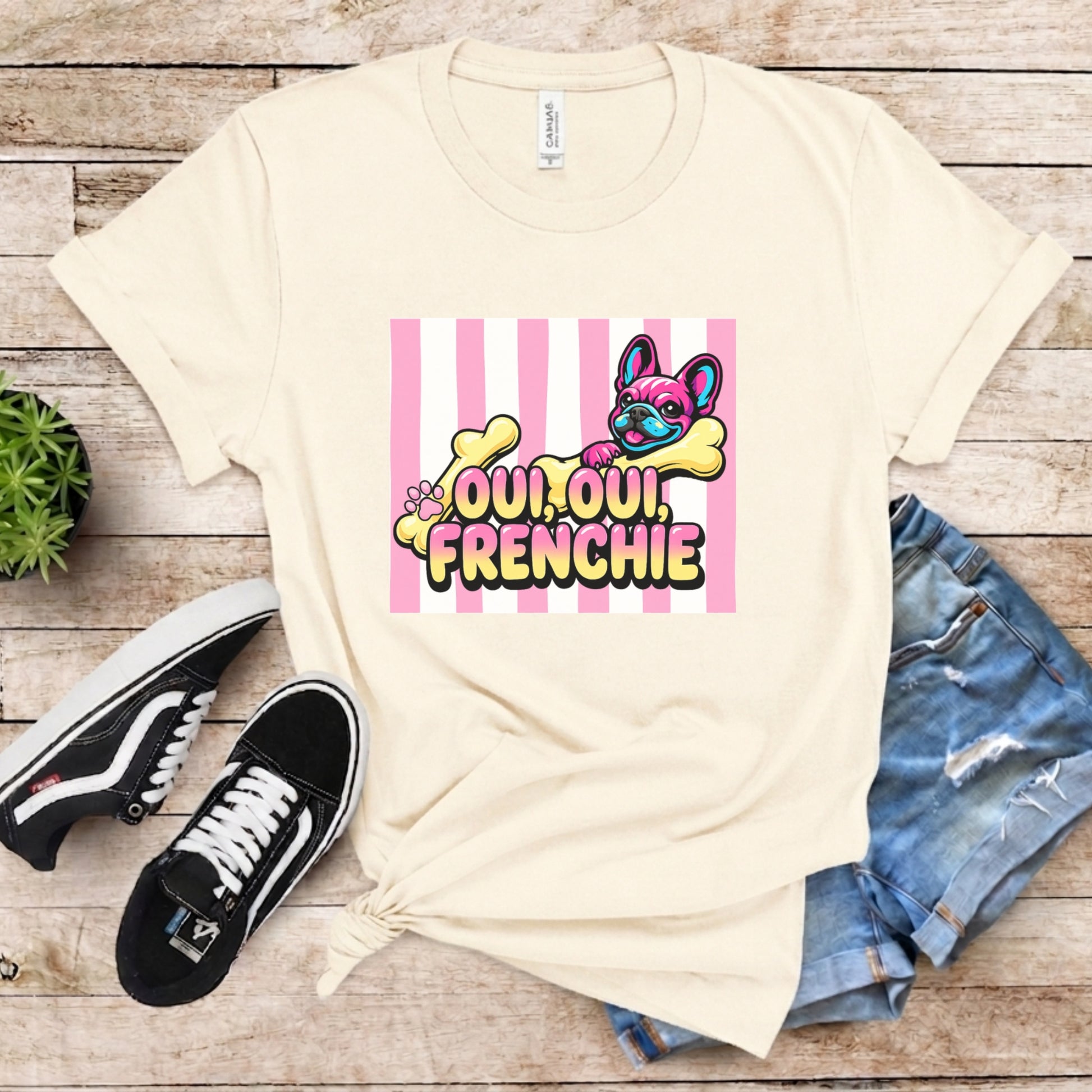 Beige t-shirt with 'Oui Oui, Frenchie' design on a wooden surface with sneakers and jeans.