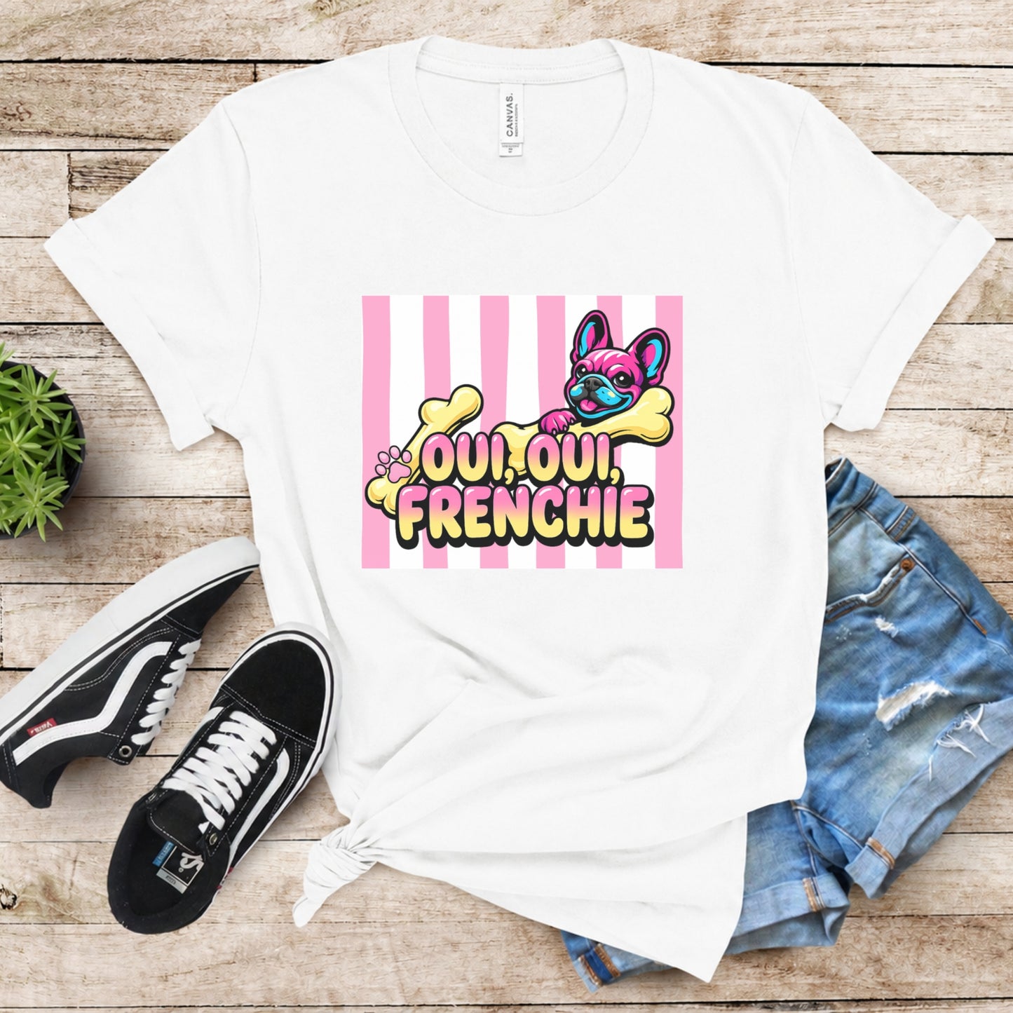 White t-shirt with 'Oui Oui, Frenchie' design on a wooden surface with sneakers and jeans.
