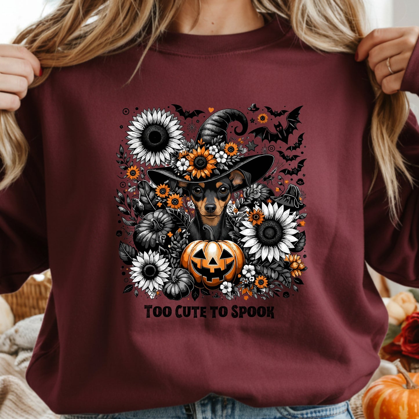 Maroon sweatshirt with a Halloween-themed design featuring a dog in a witch hat, pumpkin, and flowers.