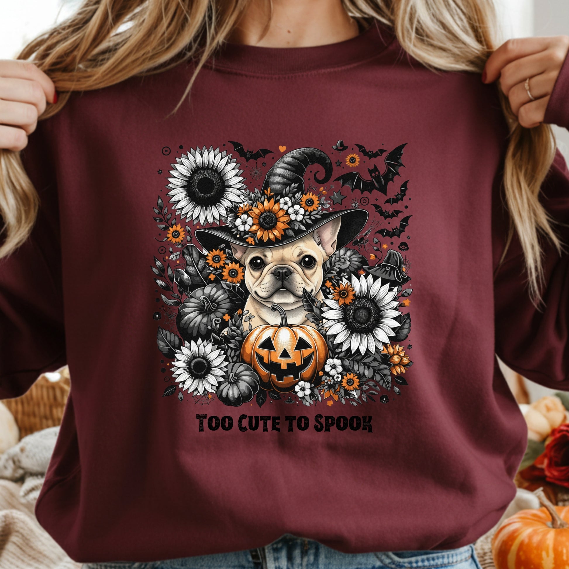 Maroon sweatshirt with a dog wearing a witch hat and pumpkin design, surrounded by flowers and text 'Too Cute to Spook'.
