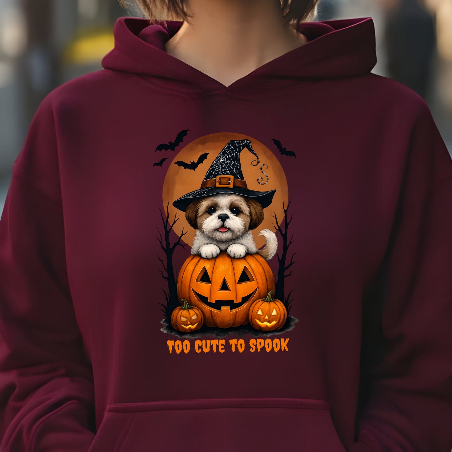 Maroon hoodie with a Halloween-themed design featuring a dog in a witch hat and pumpkin, with text 'Too Cute to Spook'.