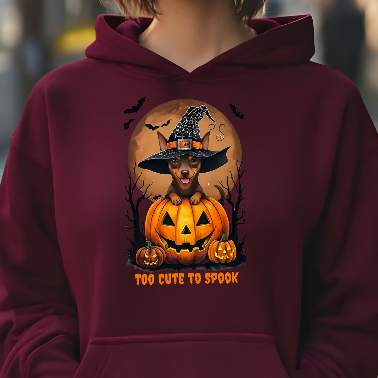 Maroon hoodie with a Halloween-themed design featuring a dog in a witch hat on a pumpkin.