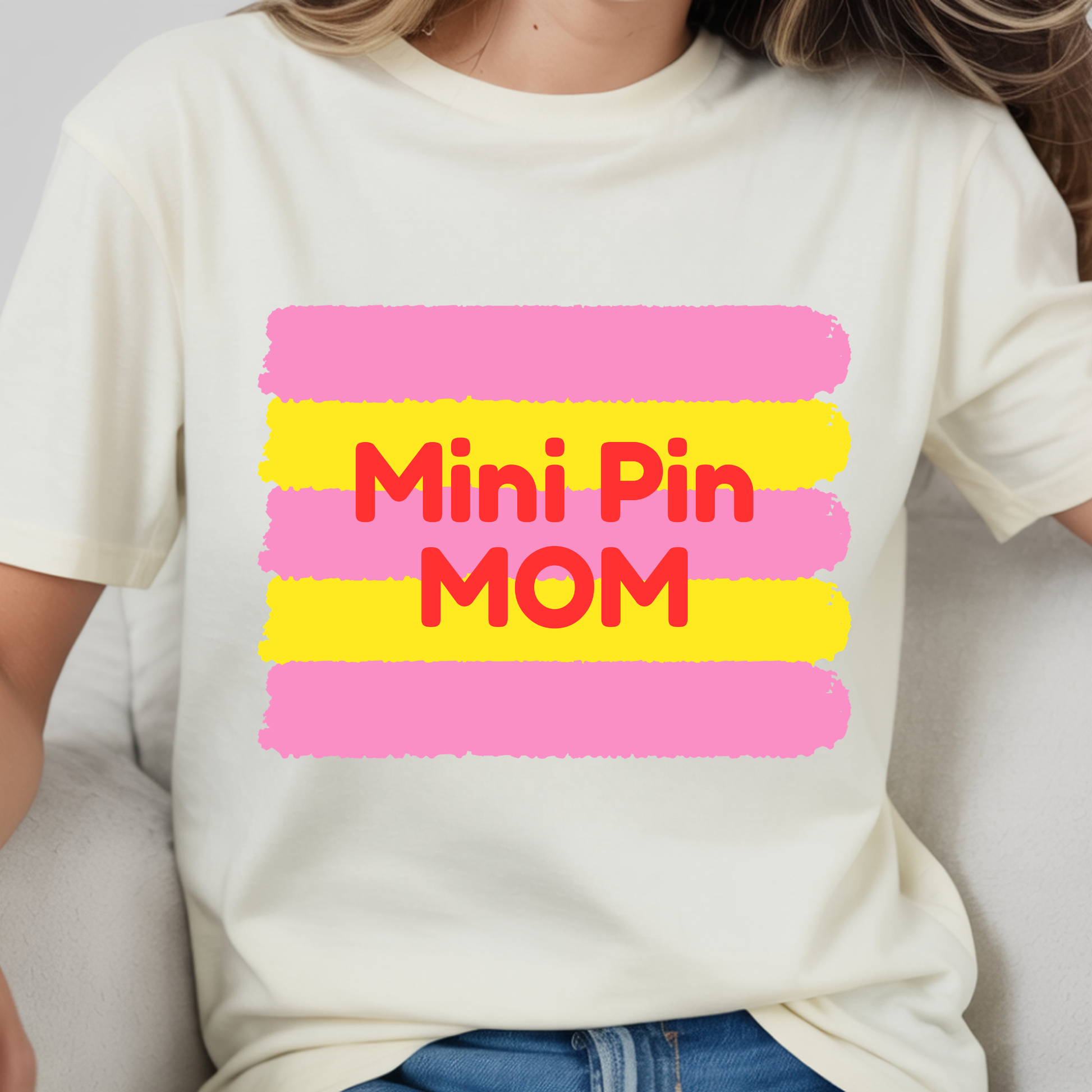 Person wearing a white t-shirt with 'Mini Pin Mom' text in red and pink on a yellow background.