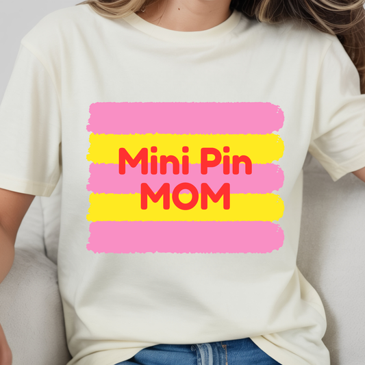 Person wearing a white t-shirt with 'Mini Pin Mom' text in red and pink on a yellow background.