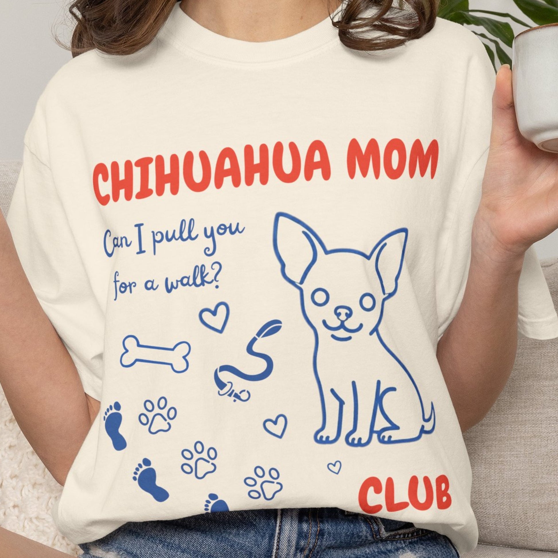 Person wearing a t-shirt with 'Chihuahua Mom Club' design, holding a cup.