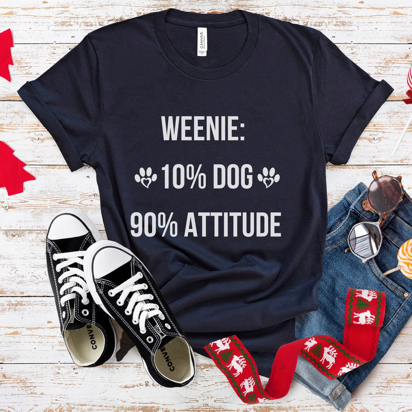 Black t-shirt with 'Weenie: 10% Dog, 90% Attitude' text, black sneakers, jeans, and socks on a wooden surface.