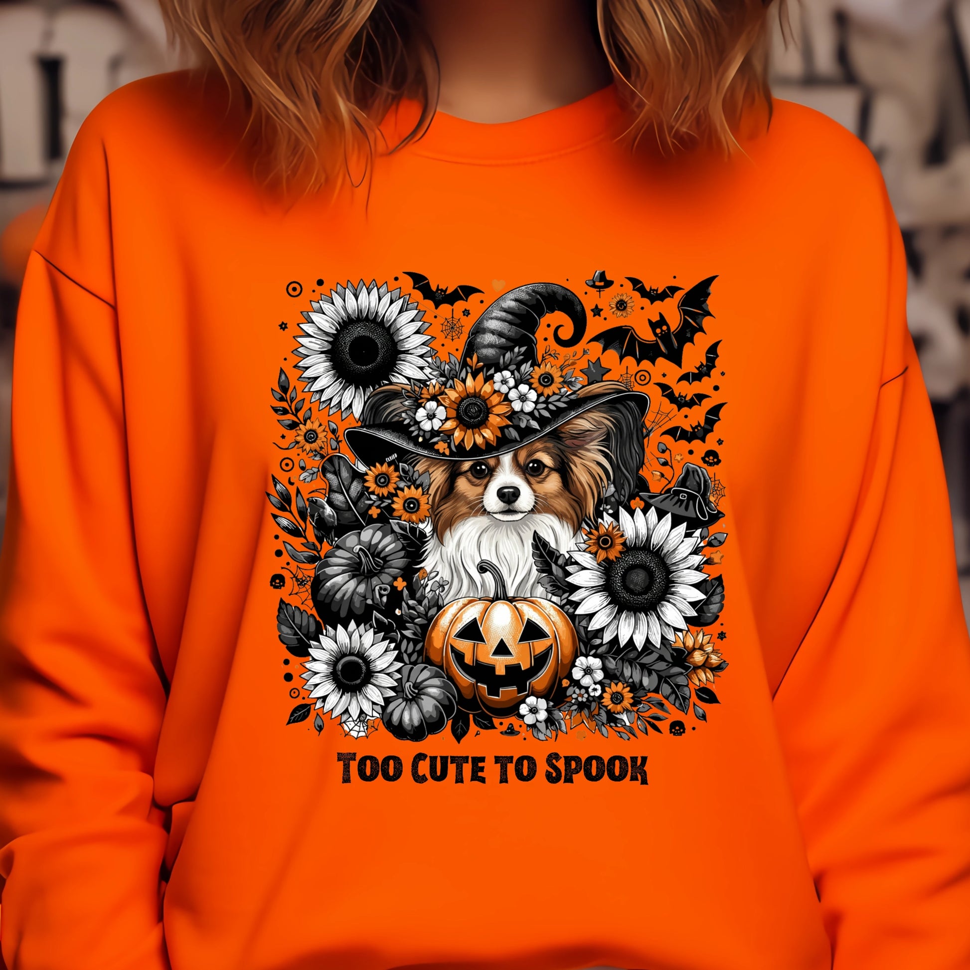 Orange sweatshirt with a Halloween-themed design featuring a dog in a witch hat, pumpkins, and flowers.