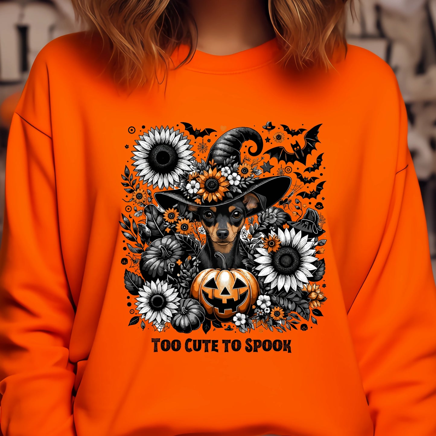 Orange sweatshirt with Halloween-themed design featuring a dog in a witch hat, pumpkin, and flowers.