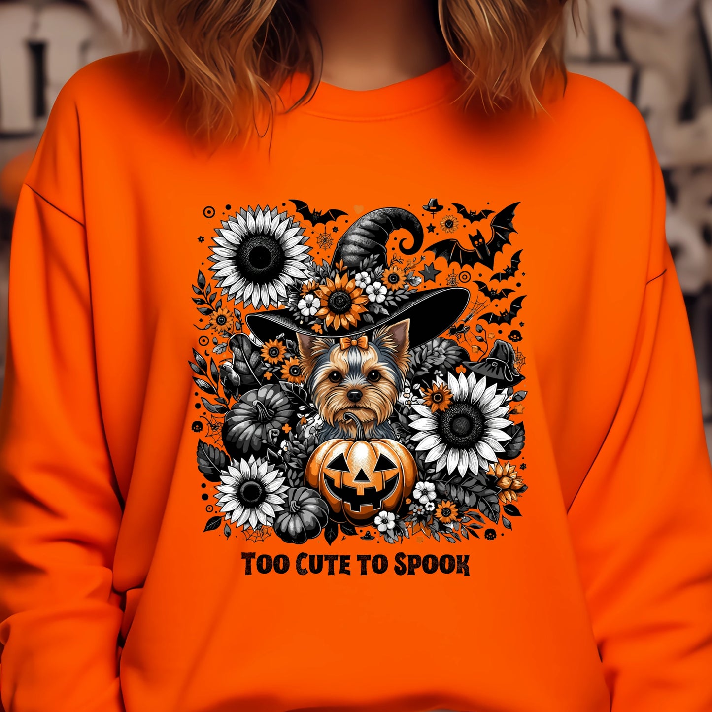 Orange sweatshirt with a Halloween-themed design featuring a dog in a witch hat, pumpkins, and flowers.