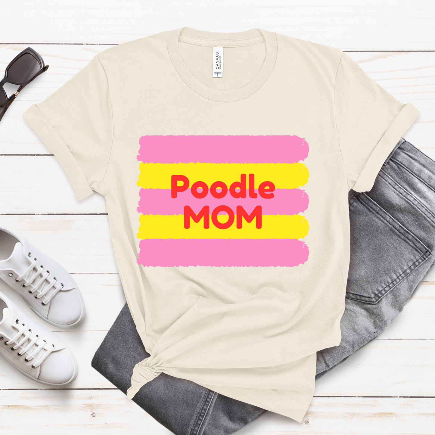 Beige t-shirt with 'FRENCHIE MOM' text on a wooden surface with shoes and jeans.