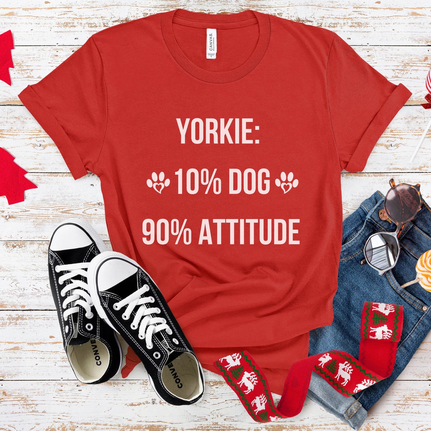 Red t-shirt with 'Yorkie: 10% dog, 90% attitude' text, black sneakers, sunglasses, and jeans on a wooden surface.