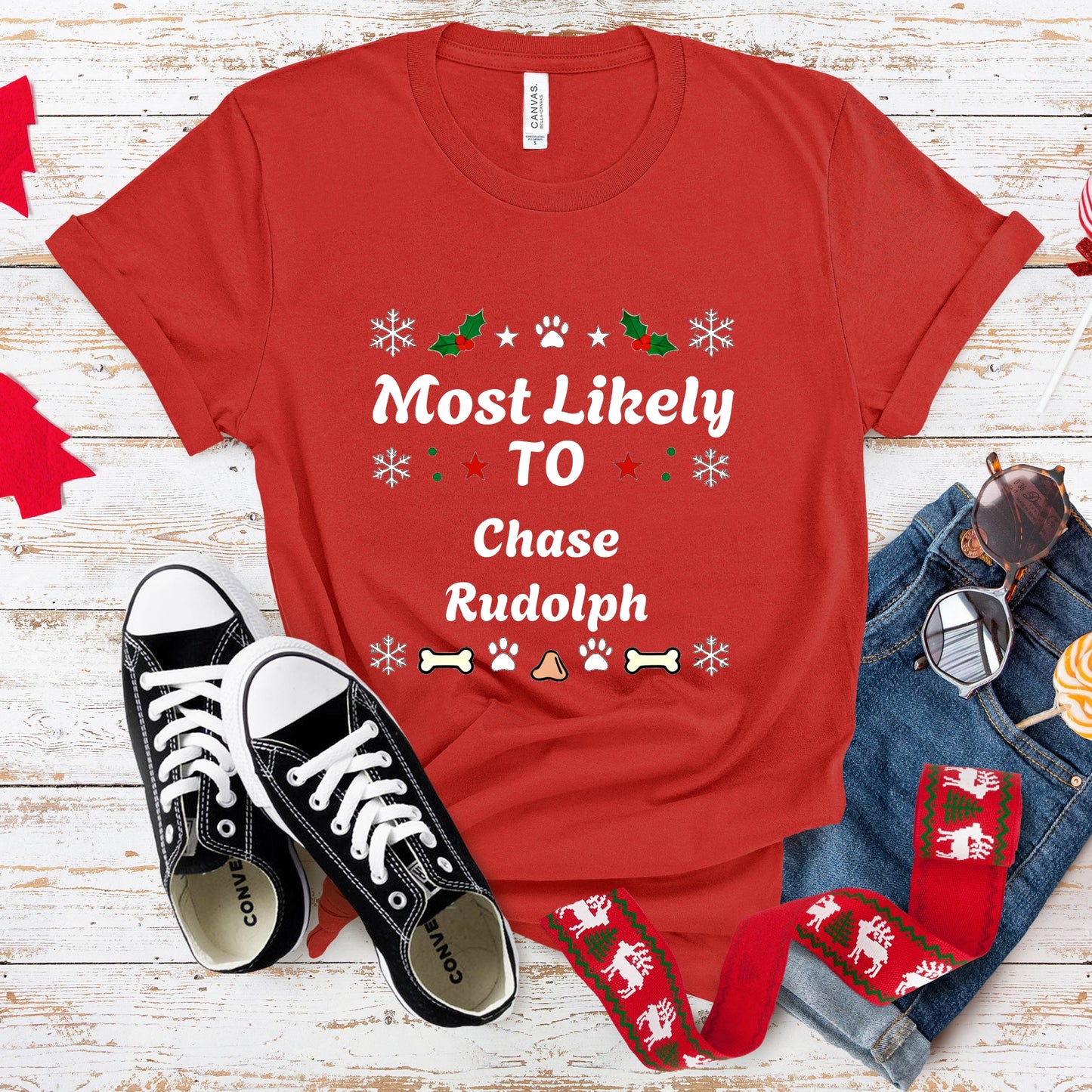 Red t-shirt with Christmas-themed text, black sneakers, and festive accessories on a wooden surface.