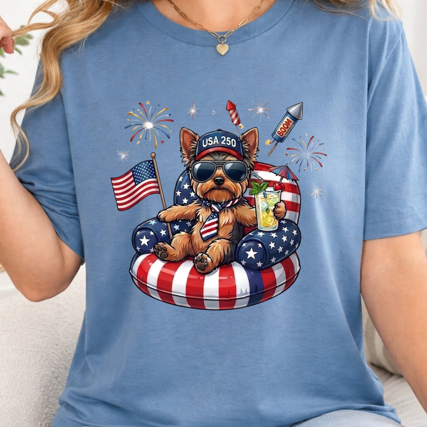 Blue t-shirt with a bear graphic wearing sunglasses, an American flag shirt, and a drink, set against a white background.