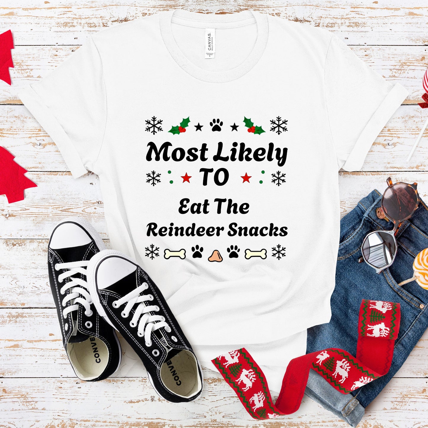 White t-shirt with Christmas-themed text, black sneakers, and festive scarf on a wooden surface.