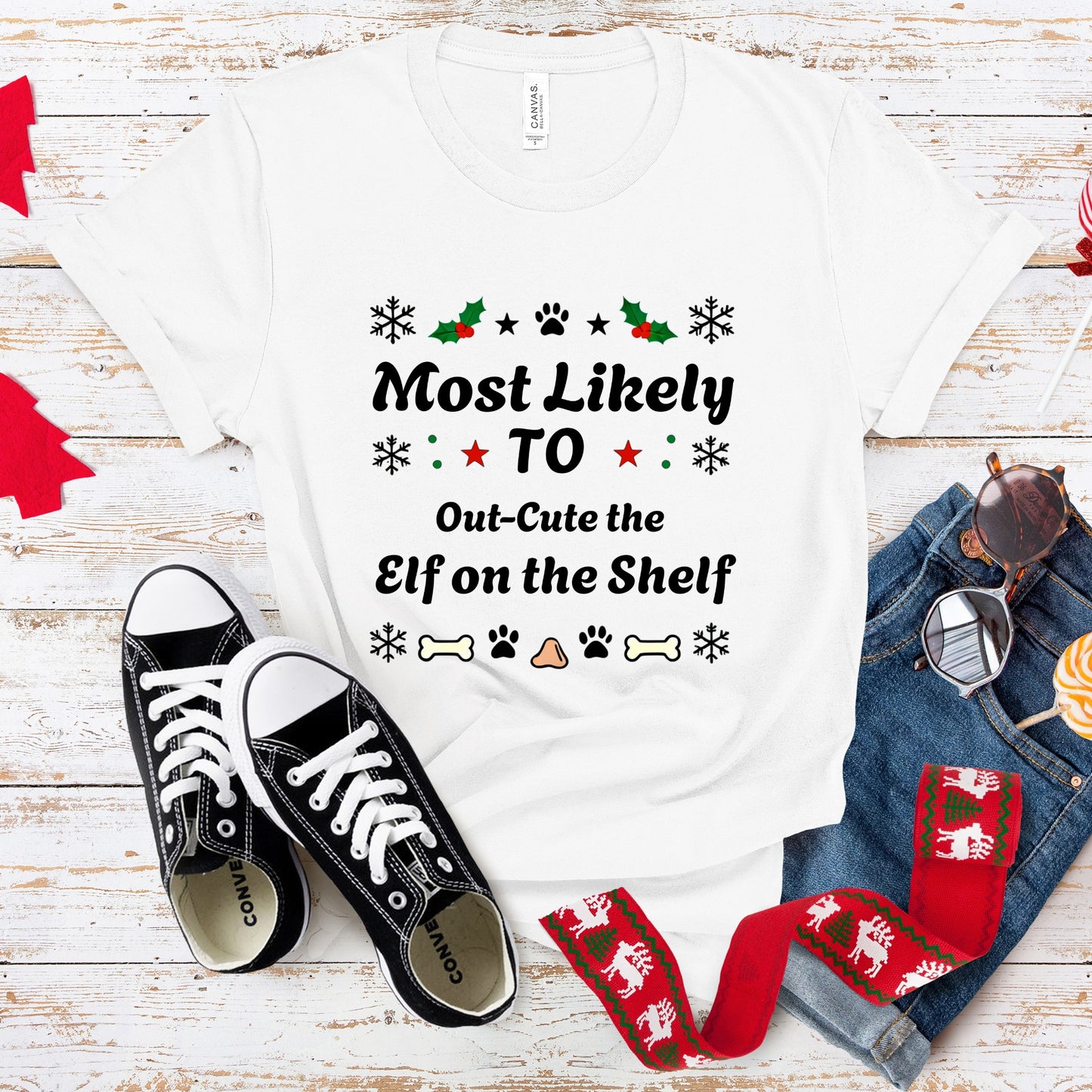 White t-shirt with Christmas-themed text, black sneakers, and festive scarf on a wooden surface.