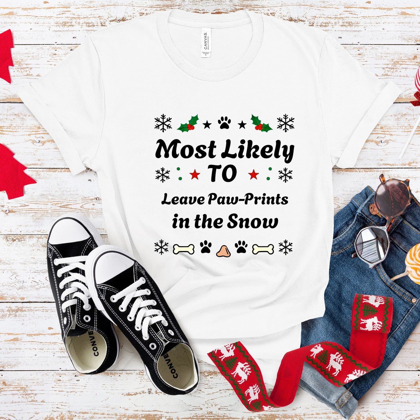 White t-shirt with Christmas-themed text, black sneakers, and festive scarf on a wooden surface.