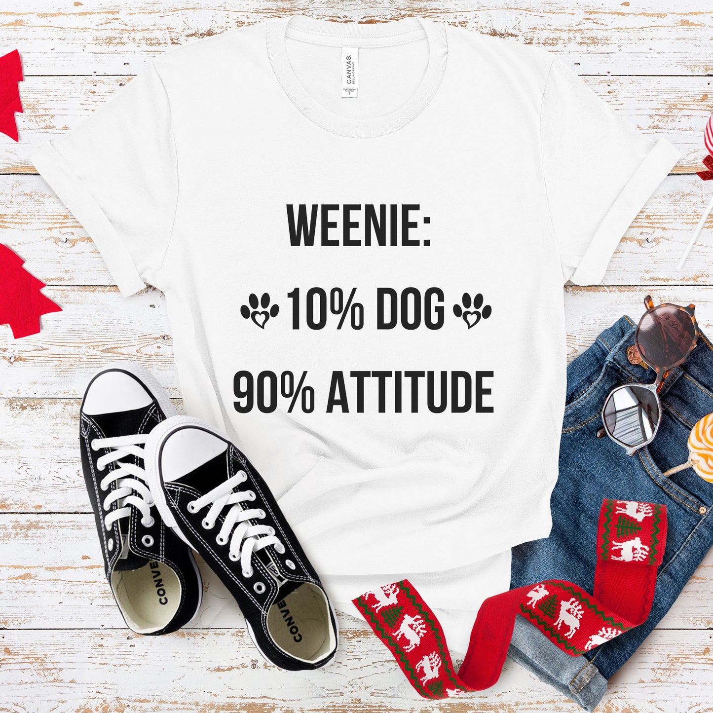 White t-shirt with 'Weenie: 10% Dog 90% Attitude' text, black sneakers, red and green patterned dog leash, and jeans on a wooden surface.