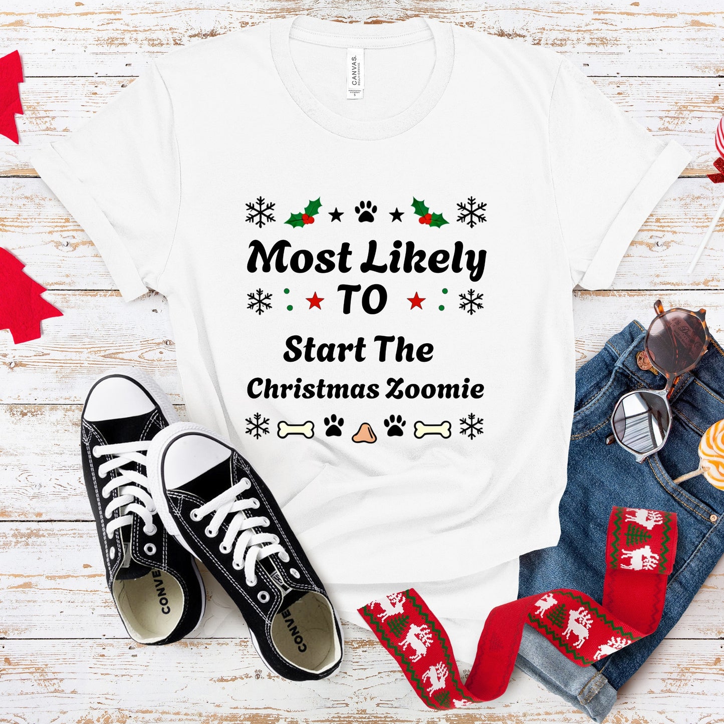 White t-shirt with Christmas-themed text, black sneakers, and festive socks on a wooden surface.