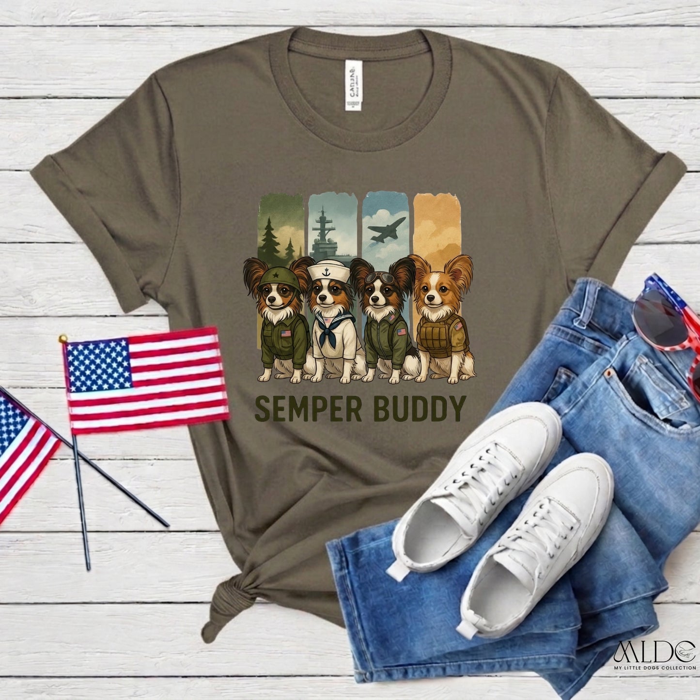 Olive green t-shirt with 'Semper Buddy' graphic, American flags, jeans, and sneakers on a wooden surface.