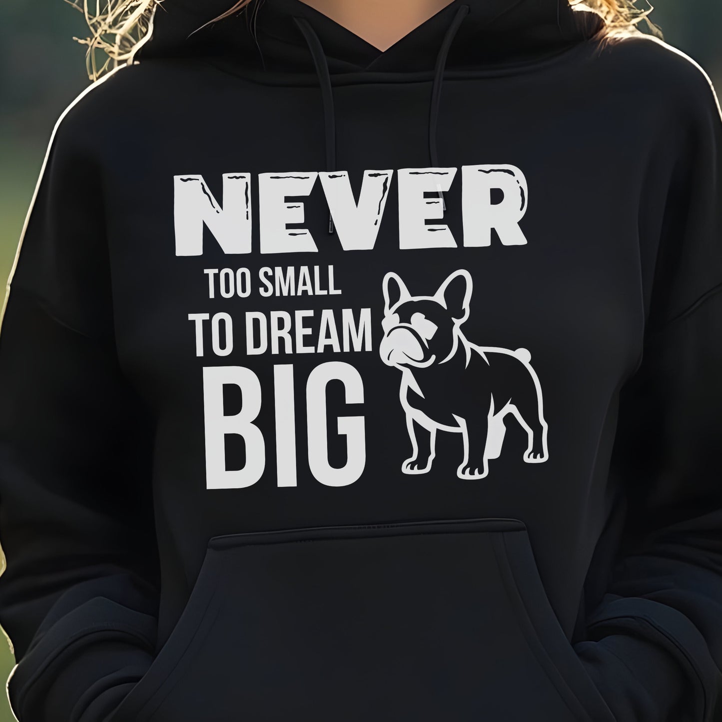 Black hoodie with a dog graphic and text 'Never Too Small to Dream Big' on a blurred natural background