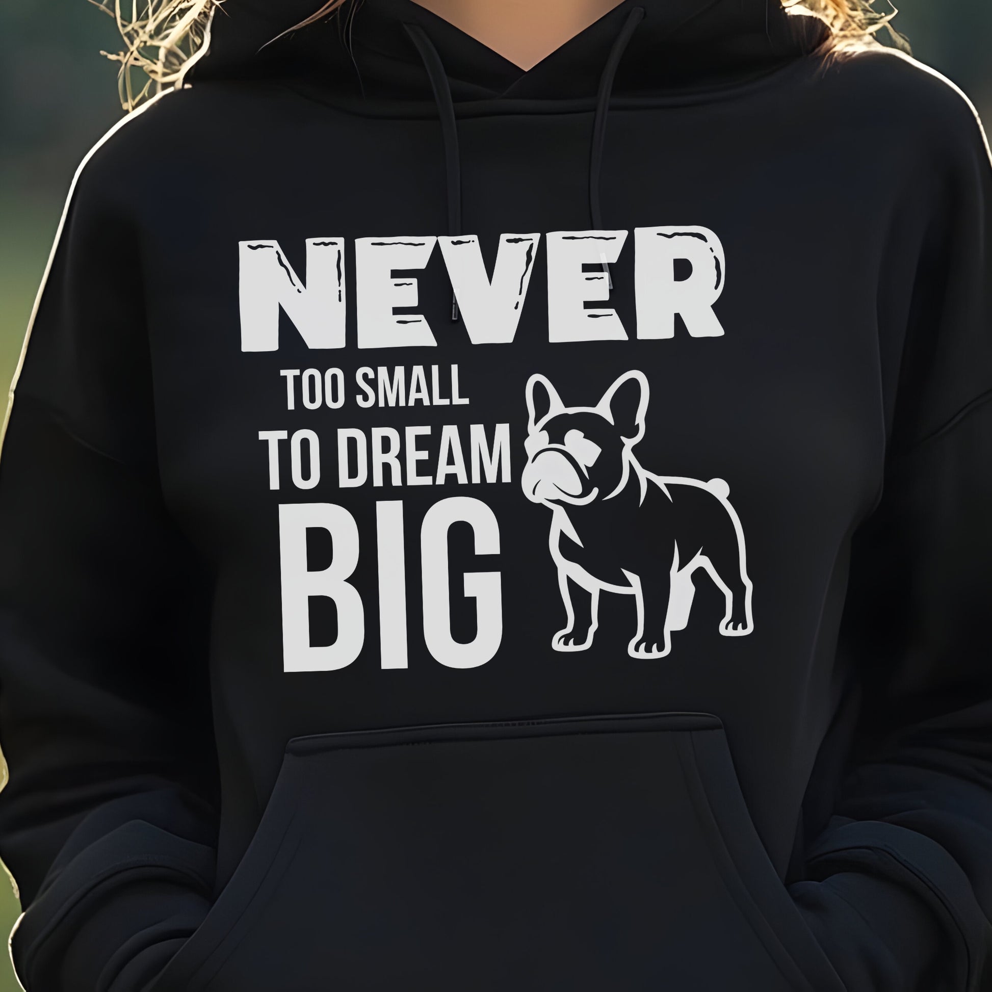 Black hoodie with a dog graphic and text 'Never Too Small to Dream Big' on a blurred natural background