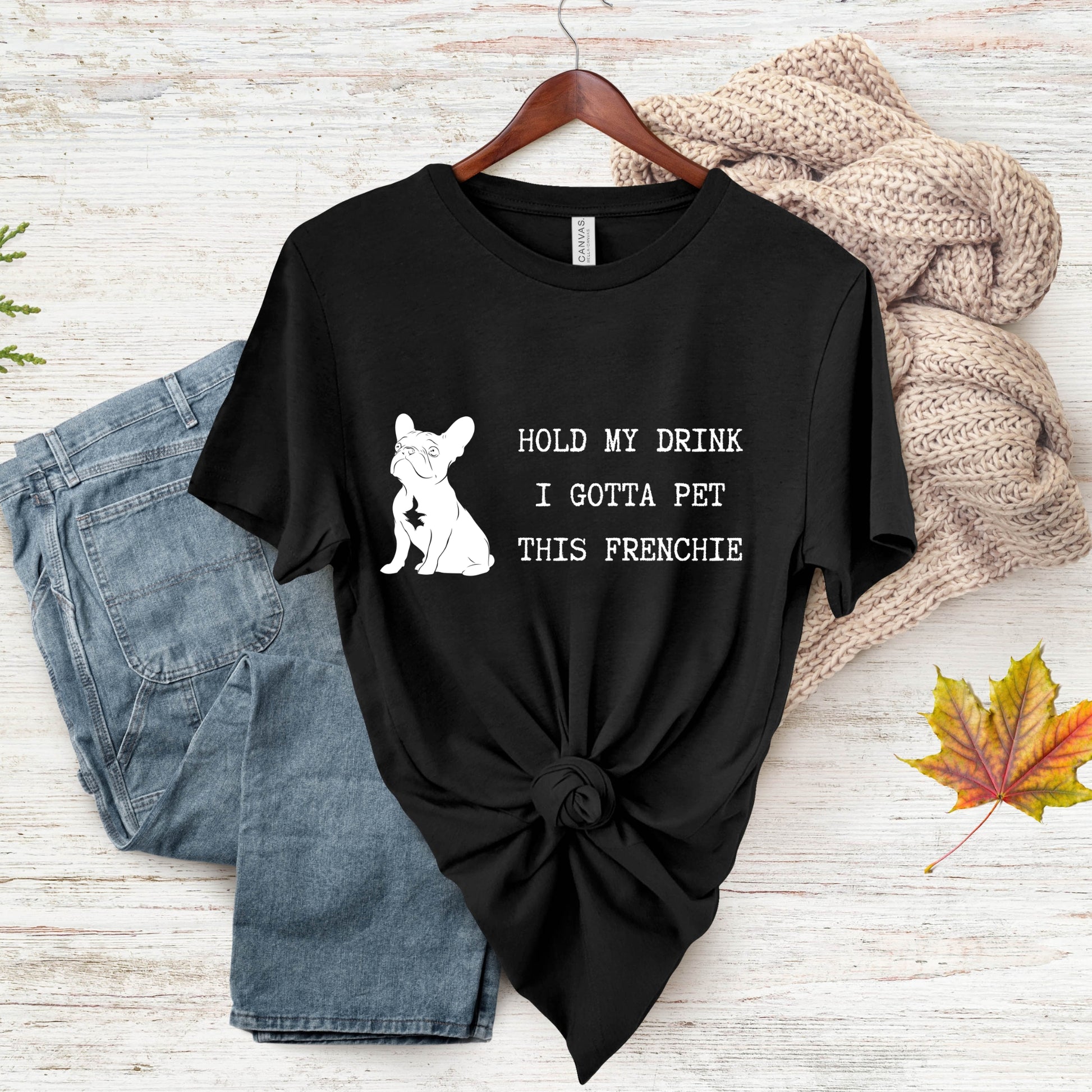 Black t-shirt with a dog graphic and text on a wooden surface with jeans and a sweater.