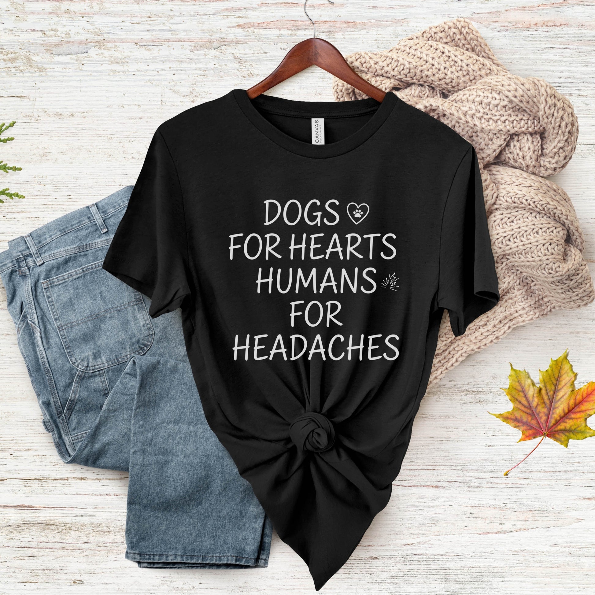Black t-shirt with 'Dogs for hearts, humans for headaches' text on a wooden surface with jeans and a sweater.