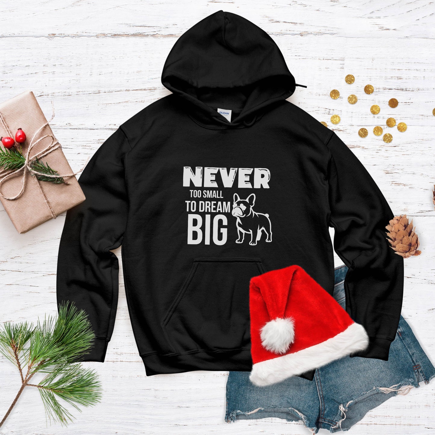 Black hoodie with text and a dog graphic, placed on a white wooden surface with festive decorations.