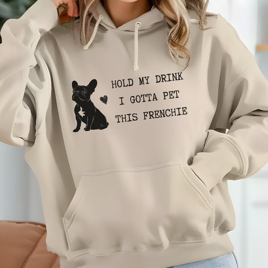 Sand hoodie with a black line-art French Bulldog illustration and the bold text “Hold my drink, I gotta pet this Frenchie” printed on the front.