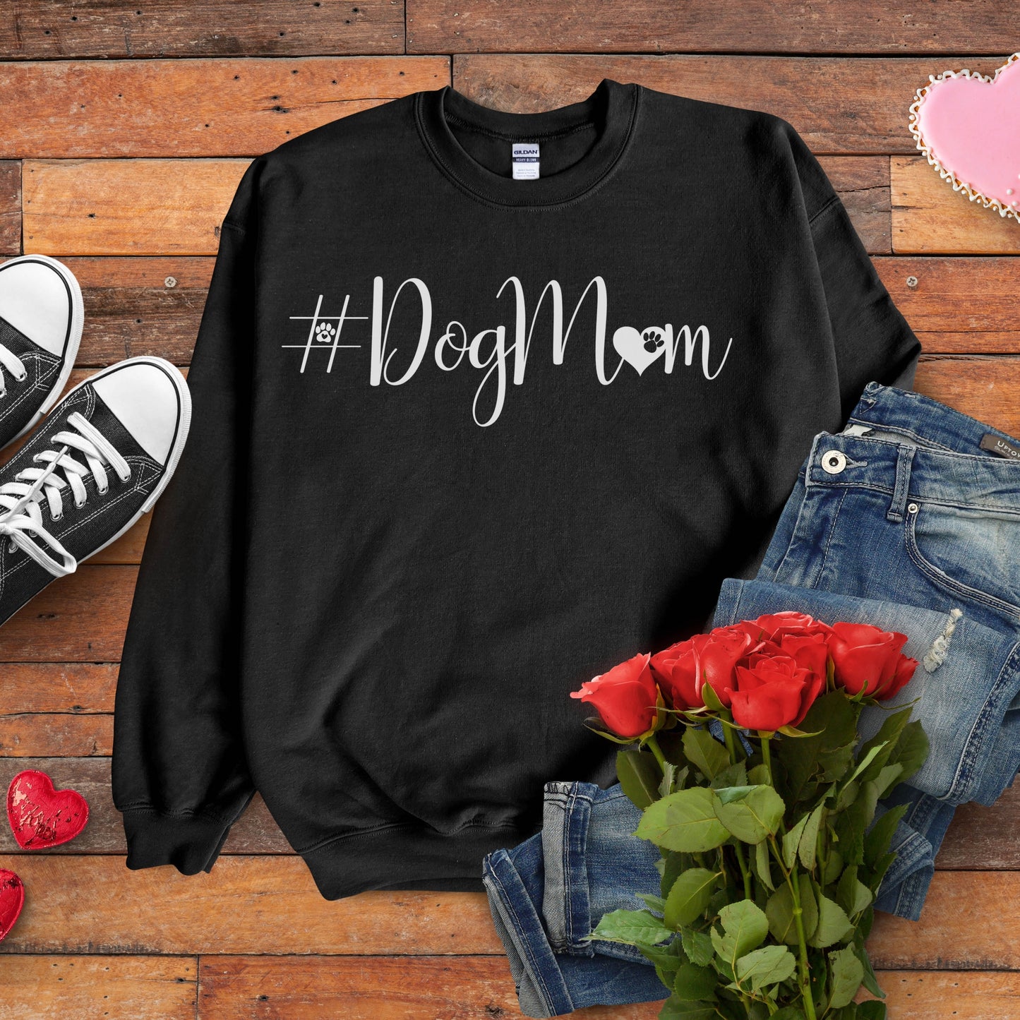 Black sweatshirt with '#DogMom' text, jeans, sneakers, and red roses on a wooden surface.
