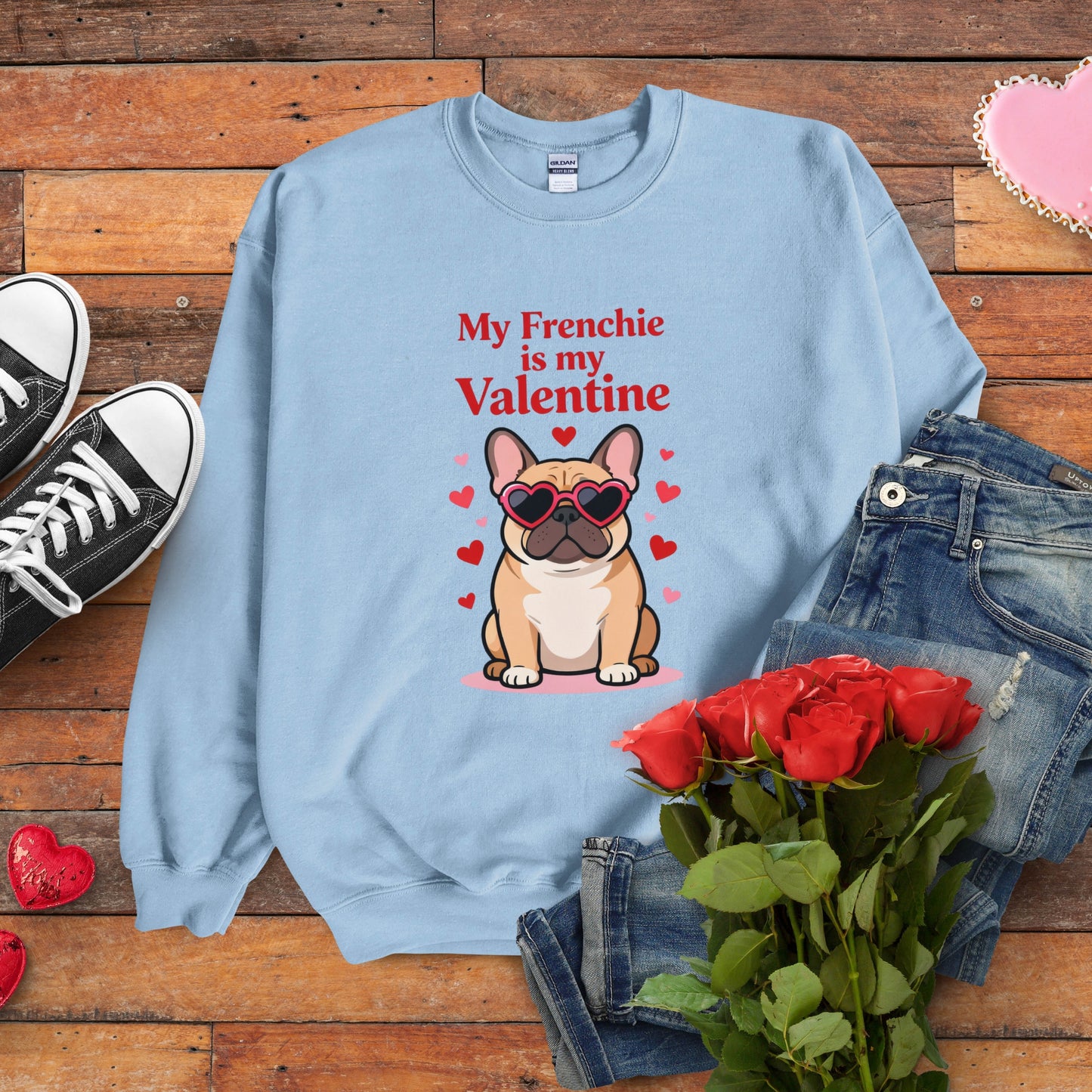 Light blue sweatshirt with a dog graphic and text on a wooden surface with jeans, roses, and sneakers.