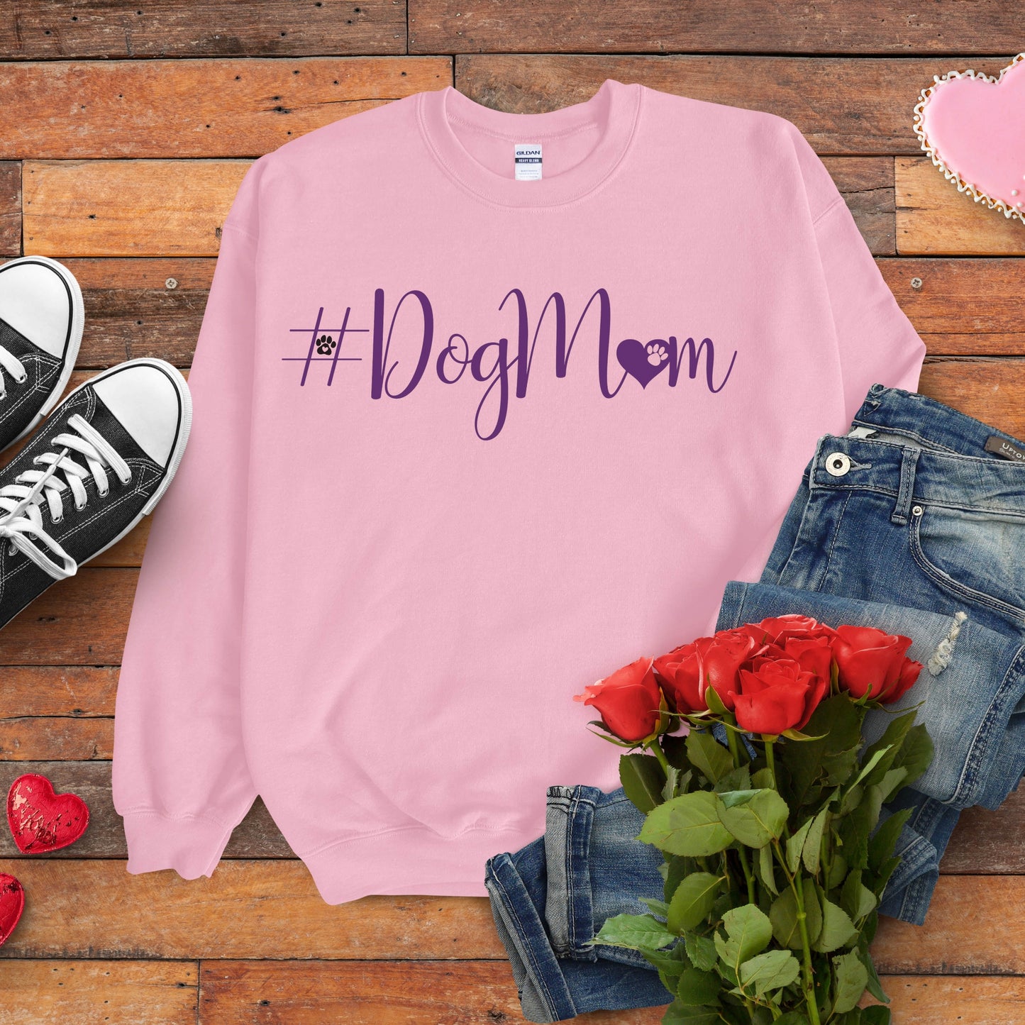 Pink sweatshirt with '#DogMom' text on a wooden surface with jeans, shoes, and roses.