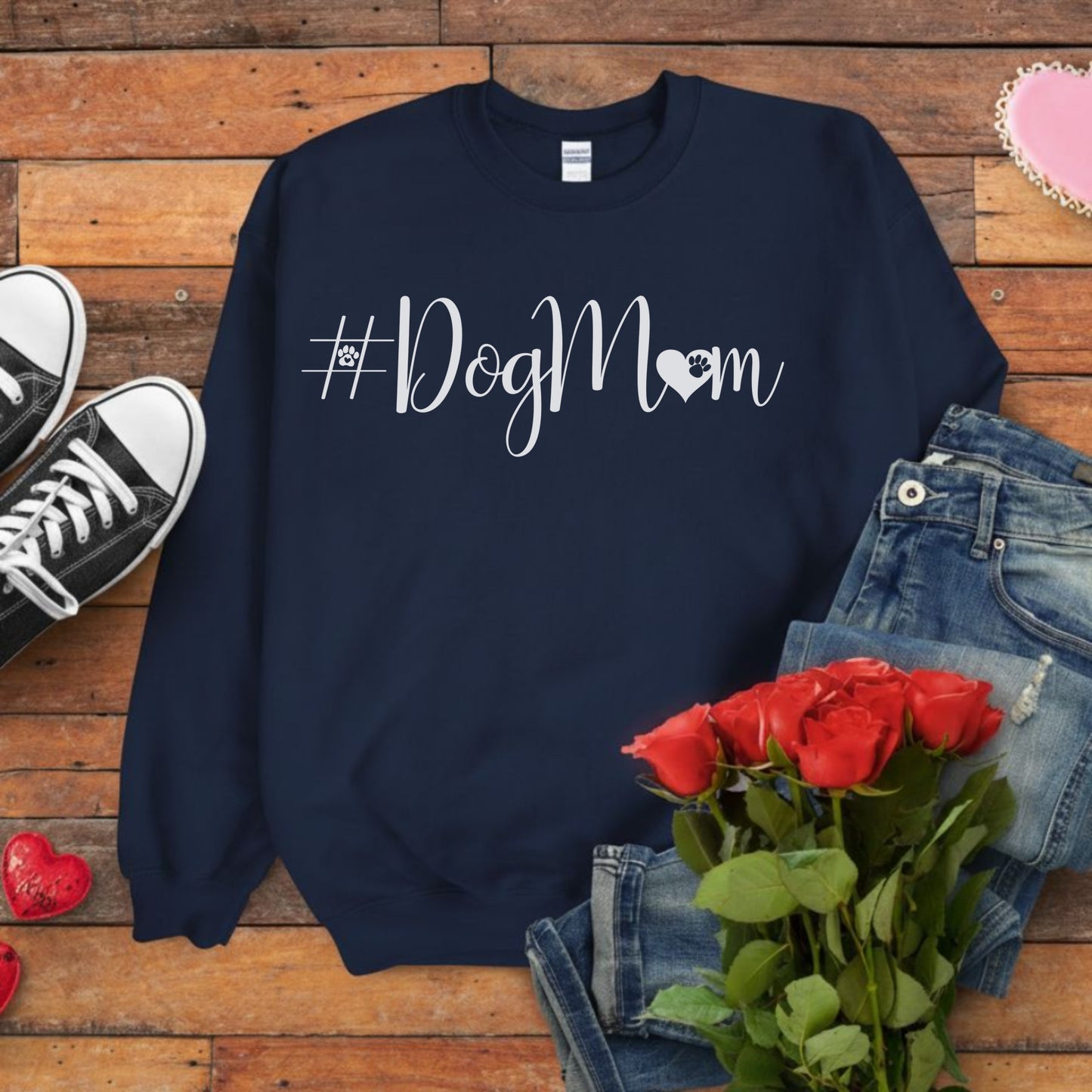 Navy blue sweatshirt with '#DogMom' text on a wooden surface with jeans, shoes, and roses.