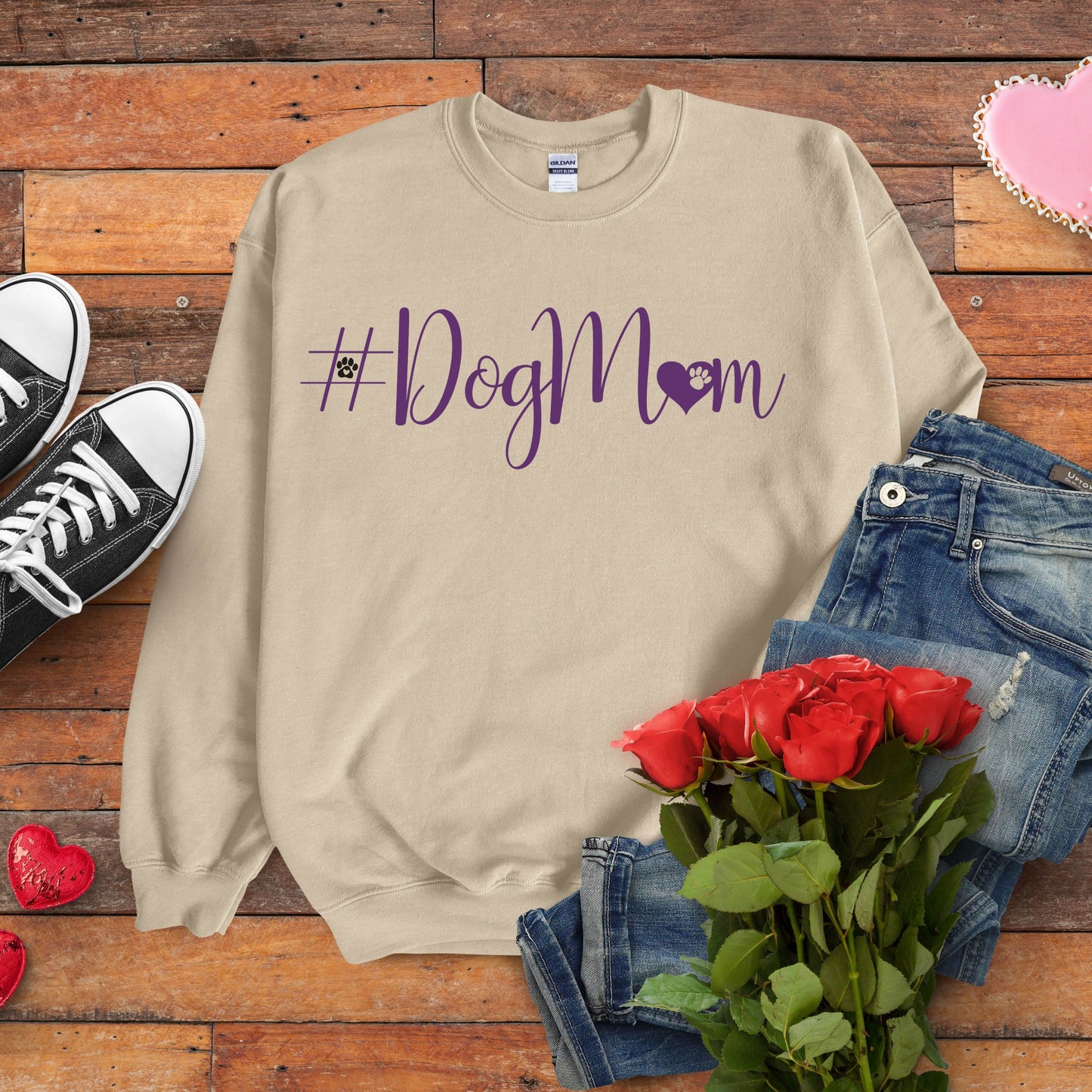 Beige sweatshirt with '#DogMom' text on a wooden surface with jeans, shoes, and roses.
